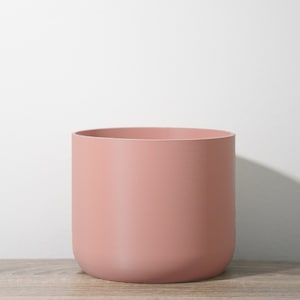 Pode incluir: Um vaso de cerâmica rosa claro com fundo arredondado e acabamento liso e fosco.