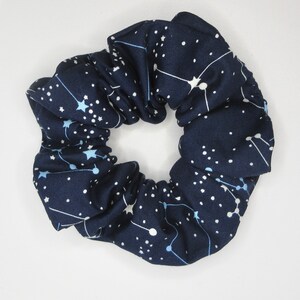 May include: A navy blue scrunchie with a white constellation pattern. The scrunchie is made of soft fabric and has a stretchy elastic band.