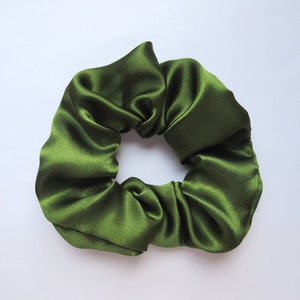 May include: A close-up shot of a dark green satin scrunchie. The hair accessory is made of a shiny, gathered fabric. The scrunchie is a solid color and appears to be new.