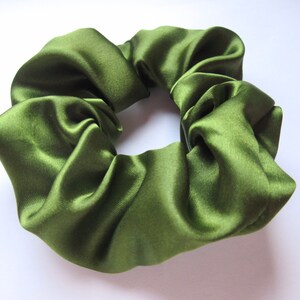 May include: Olive green satin scrunchie. This hair accessory is made of a soft, shiny fabric. The scrunchie is a circular shape, with a gathered design. The color is a rich, earthy green.