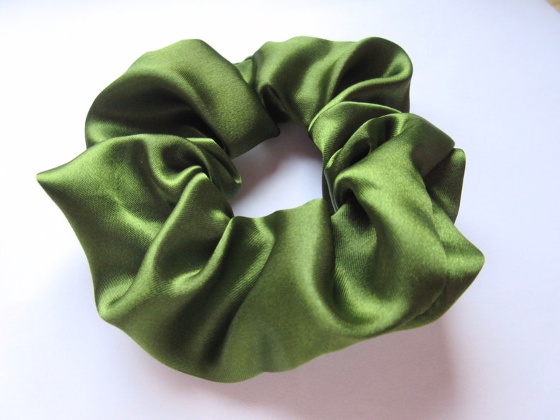 May include: Olive green satin scrunchie. This hair accessory is made of a soft, shiny fabric. The scrunchie is a circular shape, with a gathered design. The color is a rich, earthy green.