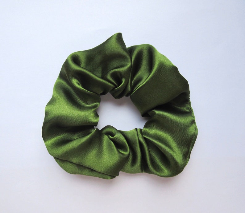 May include: A close-up shot of a dark green satin scrunchie. The hair accessory is made of a shiny, gathered fabric. The scrunchie is a solid color and appears to be new.