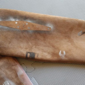 Puede incluir: Una chaqueta de ante marr&oacute;n con varios dise&ntilde;os de salpicaduras de pintura plateada y blanca. La chaqueta tiene un parche en la manga con una placa de metal.