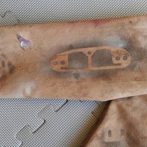 Puede incluir: Primer plano de una chaqueta de cuero marr&oacute;n con un dise&ntilde;o de plantilla en la manga. El dise&ntilde;o es un simple contorno de una pieza de autom&oacute;vil, posiblemente un colector de admisi&oacute;n.