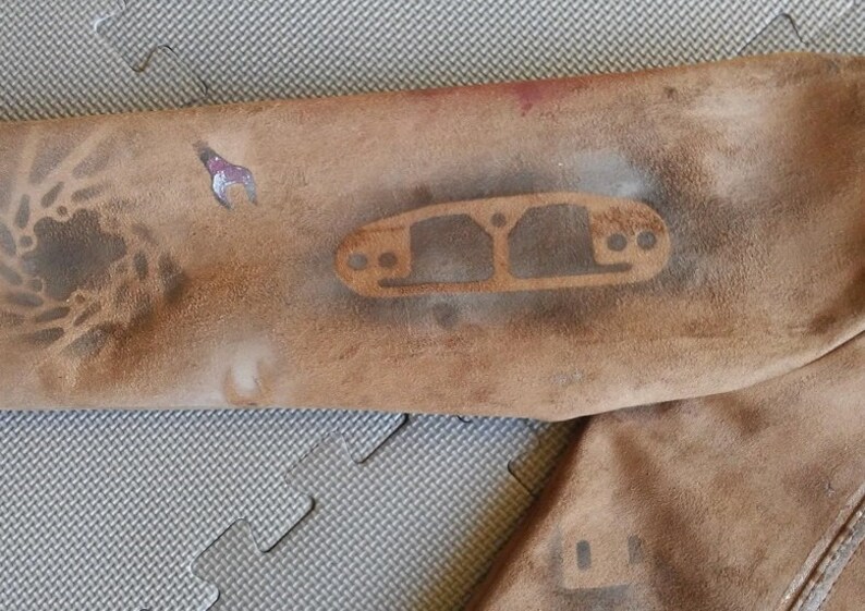 Puede incluir: Primer plano de una chaqueta de cuero marr&oacute;n con un dise&ntilde;o de plantilla en la manga. El dise&ntilde;o es un simple contorno de una pieza de autom&oacute;vil, posiblemente un colector de admisi&oacute;n.