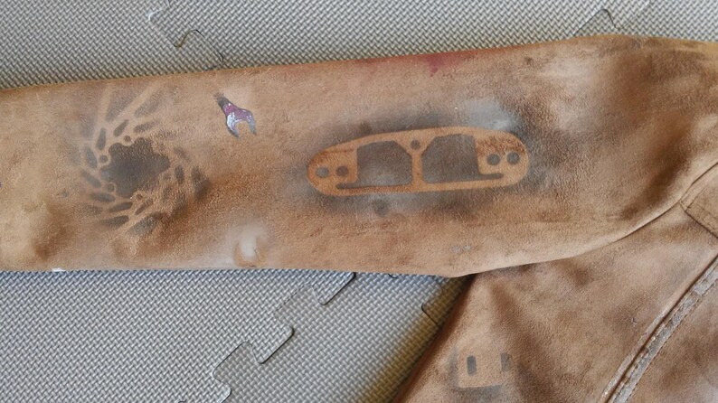 Puede incluir: Una chaqueta de ante marr&oacute;n con un aspecto desgastado. La chaqueta tiene un dise&ntilde;o de plantilla en la manga, con un patr&oacute;n circular y una forma rectangular con agujeros.