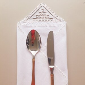 May include: A white linen napkin with a crocheted lace border, a silver knife and a gold-handled spoon.