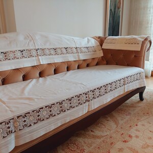 May include: A white couch with a white lace trim and a brown velvet cushion. The couch is in a room with a rug on the floor.
