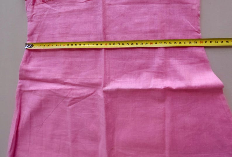 May include: A pink fabric garment with a seam down the center. A yellow measuring tape is placed across the fabric, showing a measurement of 40 inches.