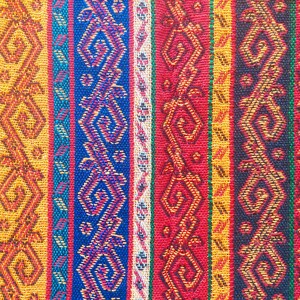 May include: Close-up of a woven textile with vertical stripes in various colors. The stripes include patterns in orange, blue, red, and yellow. The design features geometric and stylized floral motifs.