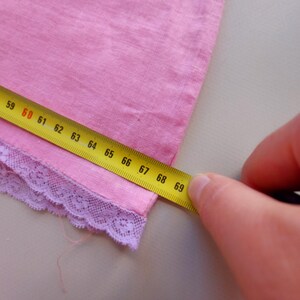 May include: A pink fabric with a purple lace trim is being measured with a yellow tape measure. The tape measure reads 59 to 69 inches.