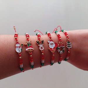 Puede incluir: Conjunto de seis pulseras con temática navideña con cuentas rojas y verdes y dijes. Los dijes incluyen un muñeco de nieve, una campana, un reno, Santa Claus, una corona y un árbol de Navidad.