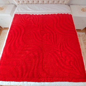 May include: A red quilted bedspread with a floral pattern. The bedspread is made of a soft, velvety fabric and has a white border.