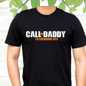 May include: Black crew neck t-shirt with the text "CALL OF DADDY FATHERHOOD OPS" in white and orange. A casual t-shirt, suitable for everyday wear.