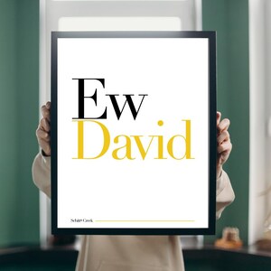 May include: A black framed print with the text "Ew. David" in yellow and black lettering. The text "Schitt's Creek" is printed in smaller black lettering at the bottom of the print.