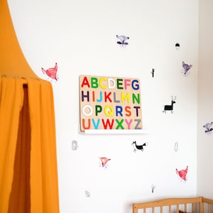 May include: A white wall with a wooden alphabet puzzle, colorful letters, and various animal stickers. The stickers include foxes, raccoons, deer, and a squirrel. There is a yellow tent canopy in the left corner of the image.