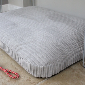 May include: A grey corduroy dog bed with a red and white rope toy on the floor.