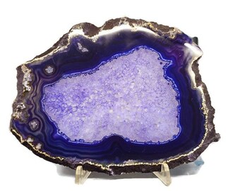 May include: A purple agate slice with a crystal center, displayed on a gold metal stand. The agate has a dark blue outer edge and a light purple inner edge.