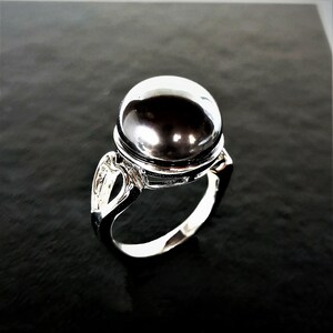 May include: A silver ring with a large, round, black gemstone. The ring has a delicate, openwork design on the band.