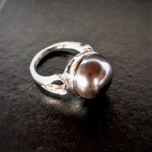 May include: A silver ring with a large, dark gray pearl set in a decorative setting.