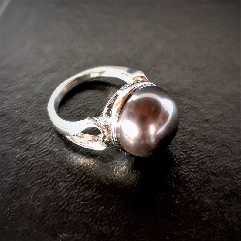 May include: A silver ring with a large, dark gray pearl set in a decorative setting.