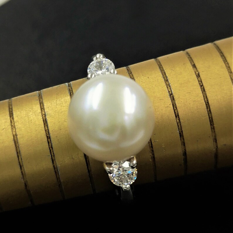 May include: A white pearl ring with three small clear diamonds set in silver.