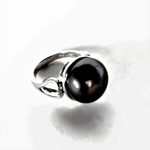 May include: A silver ring with a large black pearl. The ring has a delicate design with a curved band.