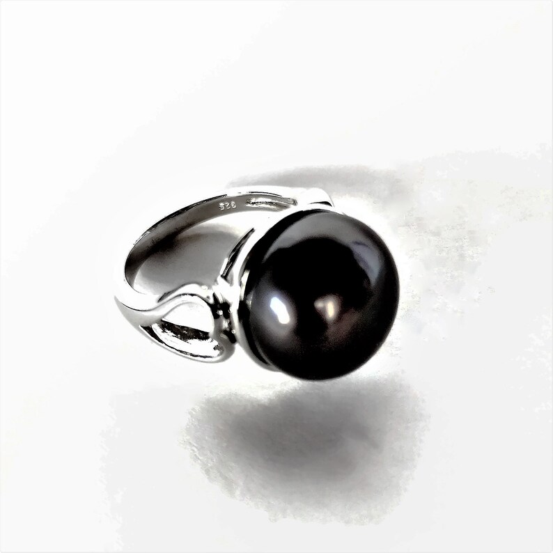May include: A silver ring with a large black pearl. The ring has a delicate design with a curved band.