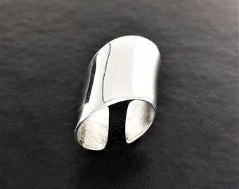 Puede incluir: Un brazalete de plata con un acabado liso y pulido. El brazalete está abierto en ambos extremos y tiene una forma ligeramente curvada.