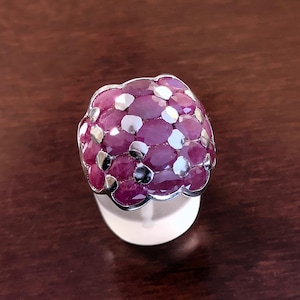 May include: A silver ring with a large cluster of oval-shaped pink gemstones. The ring is set on a white display stand.
