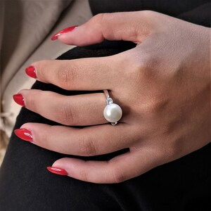 May include: A silver ring with a large white pearl and two smaller clear stones on the band.
