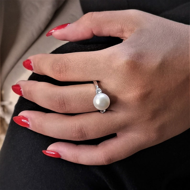 May include: A silver ring with a large white pearl and two smaller clear stones on the band.