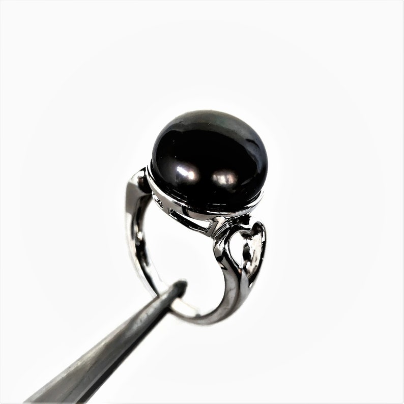 May include: A silver ring with a large black pearl set in a decorative setting.