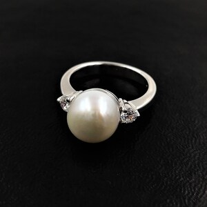 May include: A silver ring with a large white pearl and two smaller clear stones on either side.