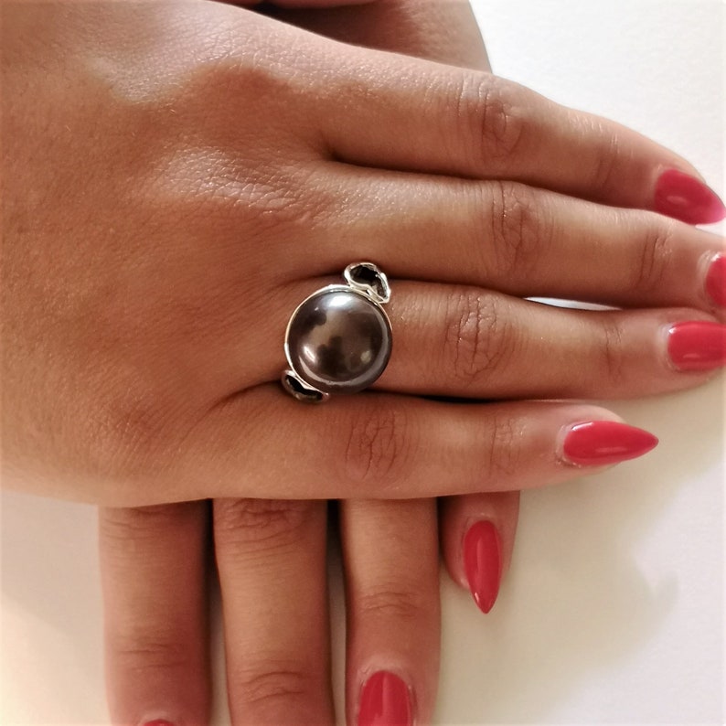 May include: A silver ring with a large, dark brown pearl set in a simple, elegant design.