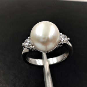 May include: A silver ring with a large white pearl and two smaller clear stones.