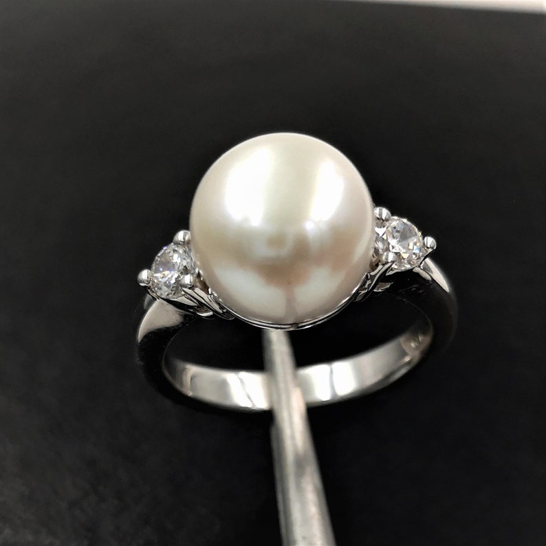 May include: A silver ring with a large white pearl and two smaller clear stones.