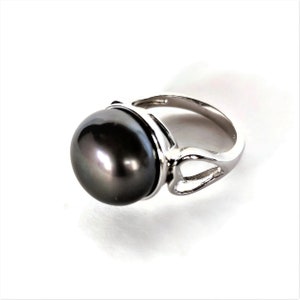 May include: A silver ring with a large, dark gray pearl set in a bezel setting. The ring has a simple, elegant design.