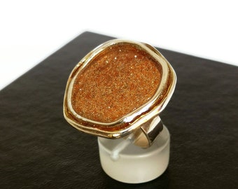May include: A gold ring with a large, irregular-shaped, brown stone set in the center. The stone is covered in tiny gold flecks.
