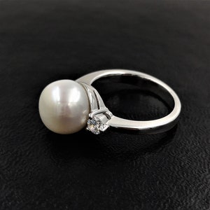 May include: A silver ring with a large white pearl and a smaller clear gemstone.