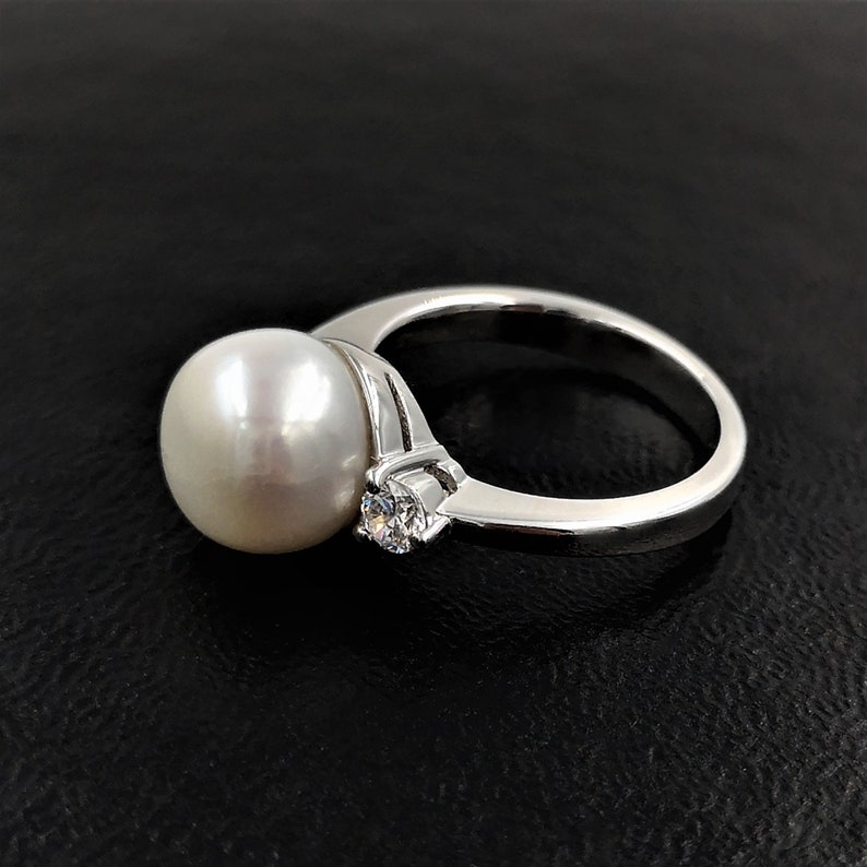 May include: A silver ring with a large white pearl and a smaller clear gemstone.