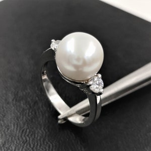 May include: A silver ring with a large white pearl and two smaller white stones on either side.