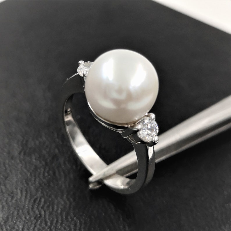 May include: A silver ring with a large white pearl and two smaller white stones on either side.