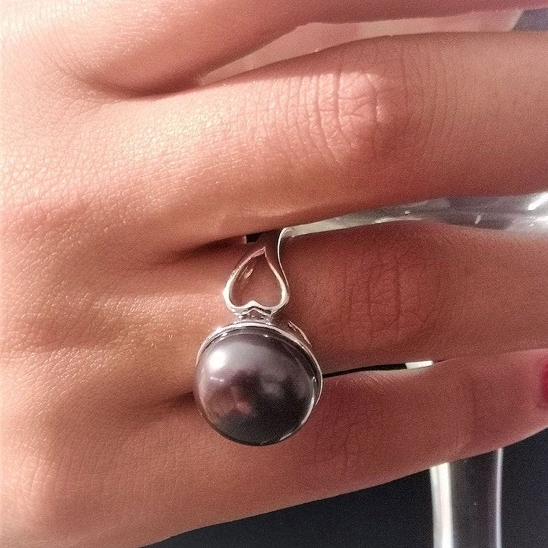 May include: A silver ring with a heart-shaped design and a large, dark pearl.
