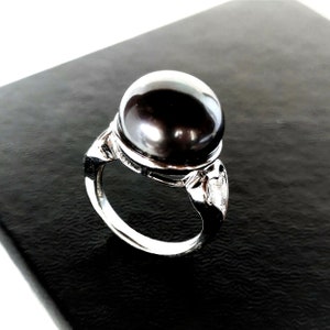 May include: A silver ring with a large black pearl set in a silver band. The ring has a decorative design on the side.