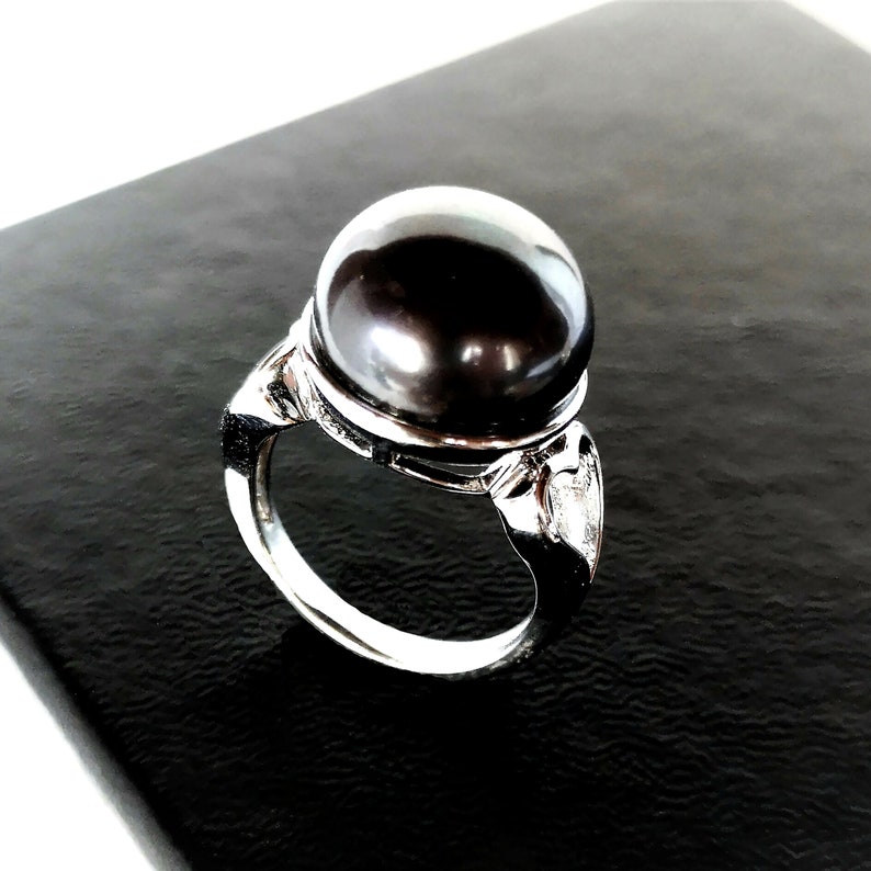 May include: A silver ring with a large black pearl set in a silver band. The ring has a decorative design on the side.