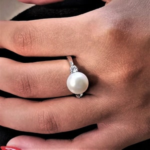 May include: A silver ring with a large white pearl and two smaller clear stones on the band.