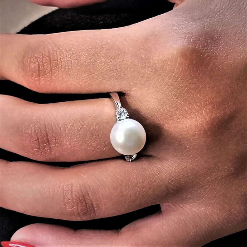May include: A silver ring with a large white pearl and two smaller clear stones on the band.