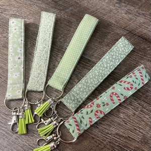 Llaveros de pulsera verde salvia, llaveros de tela con flores verde descoloridas, correas para bastón con borlas y clippers plateados.