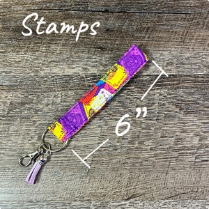 May include: A 6-inch long key fob with a colorful paisley pattern in purple, yellow, red, and blue. The key fob has a silver-colored clasp and a lavender tassel. The word "Stamps" is written in white script.